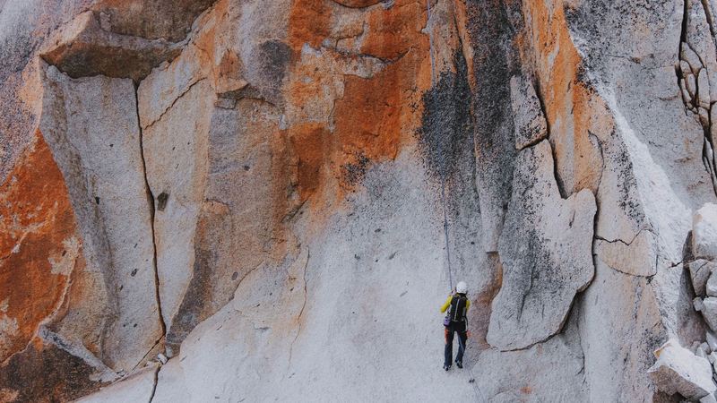 A climber in a white helmet roped up below a great wall of pale and orange rock
