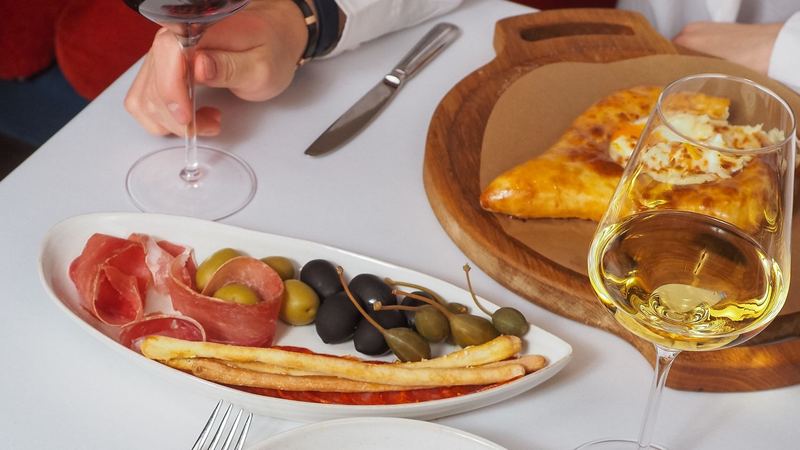 Red and white wine with cured ham, olives, grissini and grilled squid on a white tablecloth