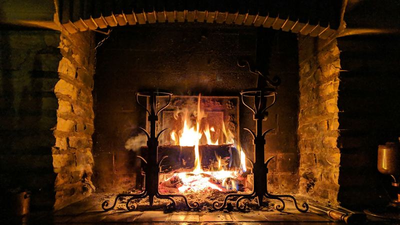 A log fire blazing in a deep stone fireplace behind wrought-iron firedogs