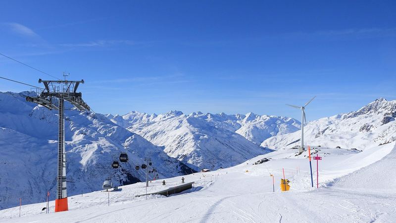 Gondolas of the SkiArena climbing above wide groomed pistes and snowy peaks under a deep blue sky