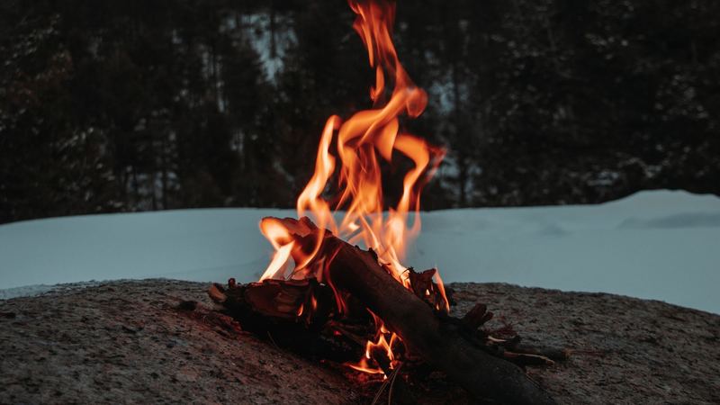 A small fire burning on a granite rock above the snow, dark forest and a stormy sky behind
