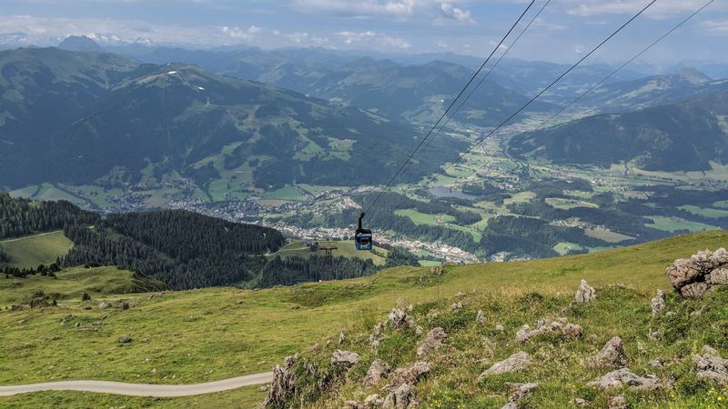 A cable car above the green summer slopes of the Kitzbüheler Horn, with Kitzbühel in the valley below