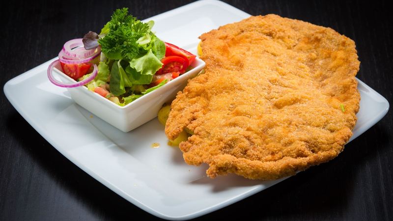 A Wiener Schnitzel with potato salad and a green salad on a white plate
