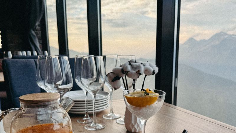 A table laid with glasses, tea and a dessert at a window high above the mountains