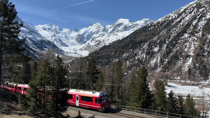 A red Rhaetian Railway train on the Bernina line below snowy peaks and a glacier