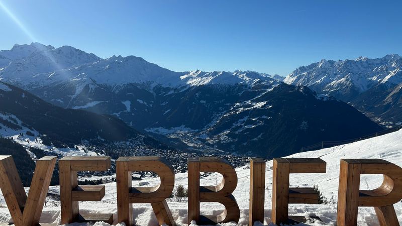 Wooden letters spelling Verbier in the snow above the valley and the peaks