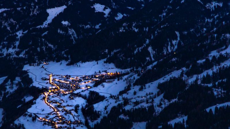 The lights of a village in the valley below Verbier at dusk, under snowy peaks
