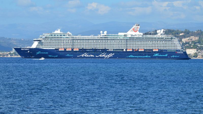 Mein Schiff 3 at anchor off a wooded coast