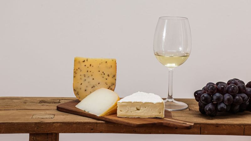 Alpine cheeses on a board on an old wooden table, a glass of white wine and black grapes beside them