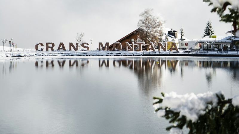 The letters CRANS MONTANA reflected in a lake after fresh snow