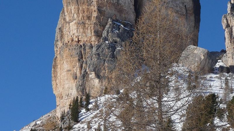 A great tower of pale rock above snowy slopes and a bare larch, under a deep blue sky
