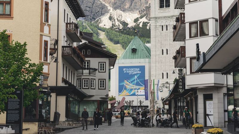 The pedestrian Corso Italia in Cortina d'Ampezzo, with shops, café tables and the green-roofed church