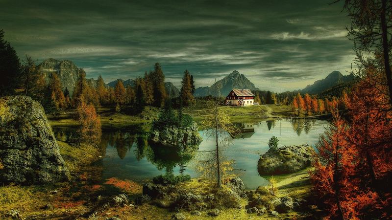 A still mountain lake with a refuge on its shore, autumn larches in red and gold around it