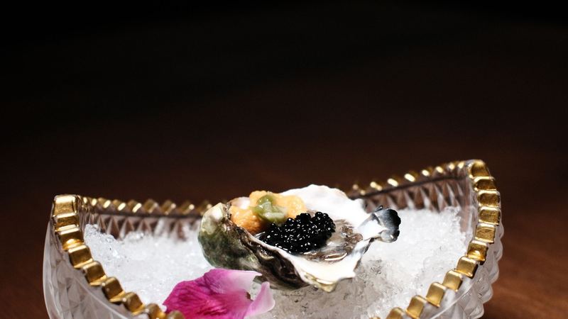 An oyster with caviar and sea urchin on crushed ice in a gold-rimmed crystal dish