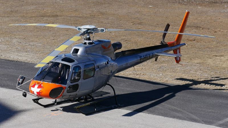 A silver and orange helicopter waiting on the apron in winter sun