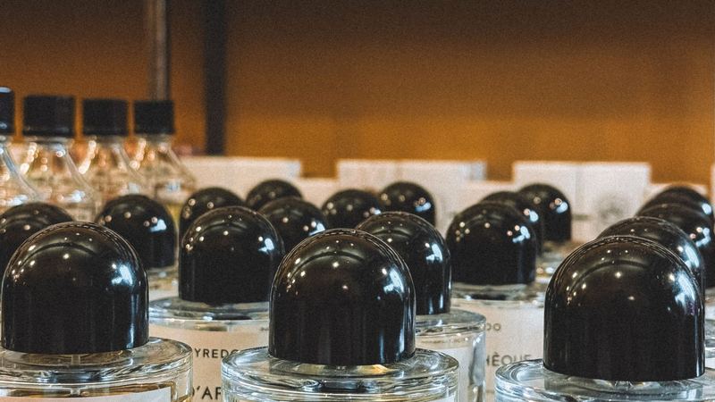Rows of perfume bottles with black caps in a perfumery, boxed scents on the shelves behind