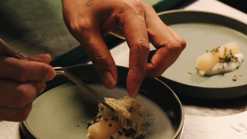 A chef finishing a delicate course with tweezers in the kitchen