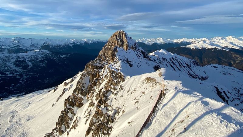 A rocky summit rising from snowy ridges above the Tarentaise, under a wide blue sky
