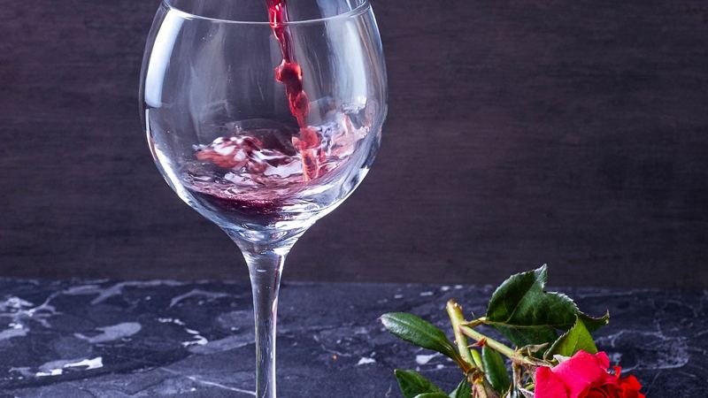 Red wine poured into a glass on dark marble beside a bunch of red roses