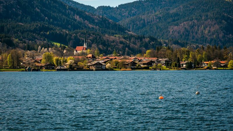 A village of chalets and a red-roofed church among blossoming trees on the shore of the Tegernsee in spring