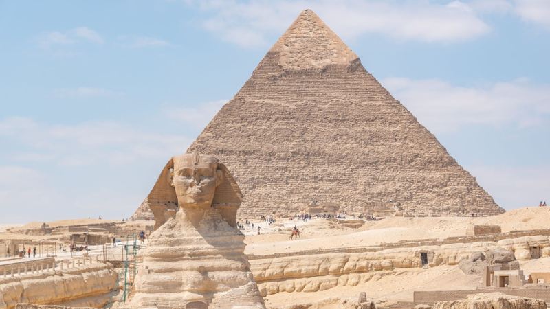 The Great Sphinx of Giza in front of the Pyramid of Khafre under a pale blue sky