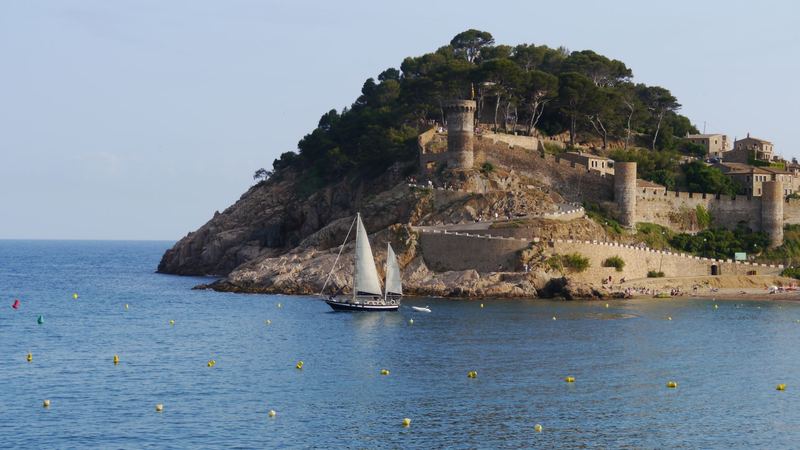 A ketch under sail below the medieval walls and towers of Tossa de Mar on the Costa Brava