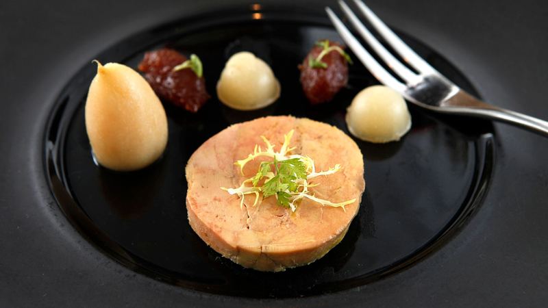 A slice of foie gras with pear and fruit chutney on a black plate