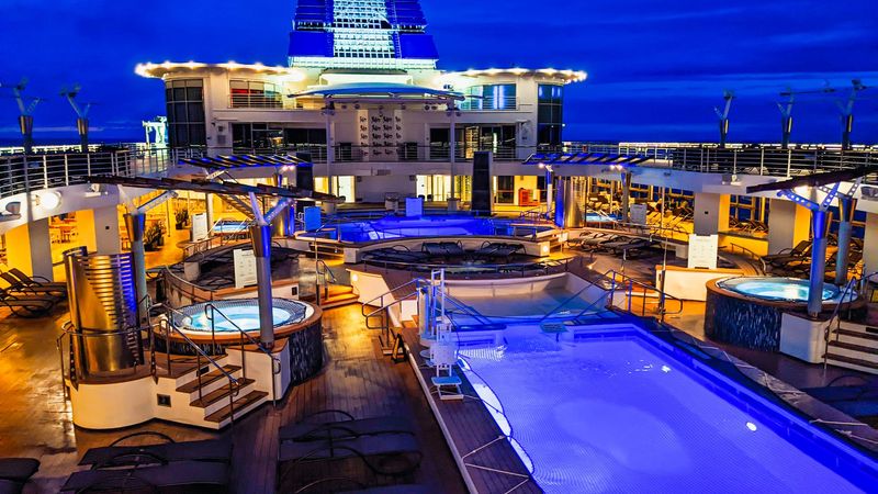 A ship’s pool deck and whirlpools lit at dusk