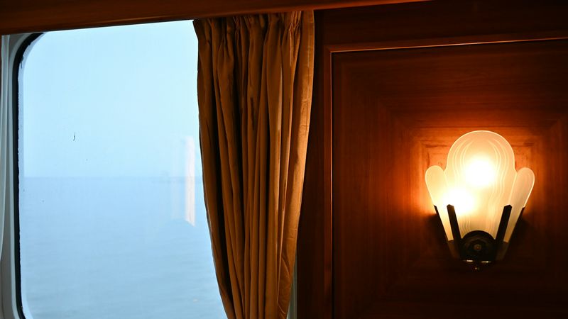 A suite window on the open sea, with a lit sconce on panelled wood