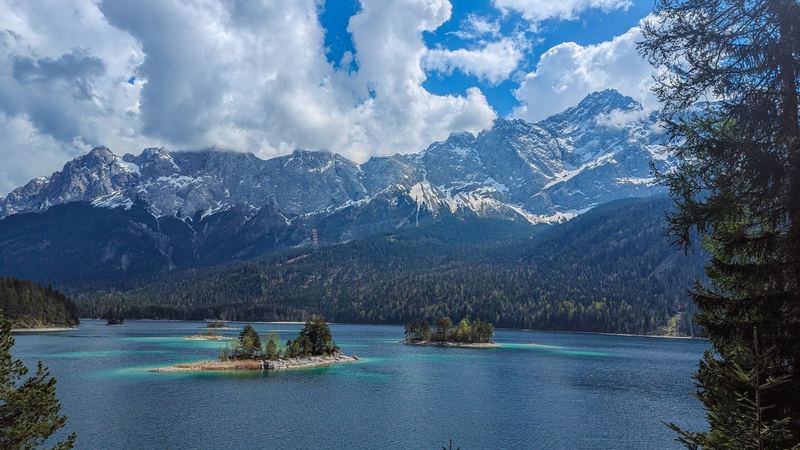 Small wooded islands in the turquoise water of the Eibsee, the Zugspitze massif beyond under white clouds