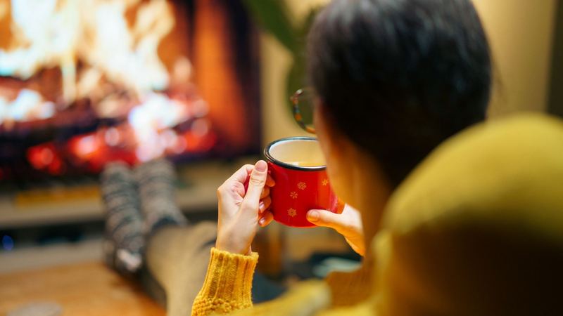 A guest in a mustard sweater with a red enamel mug, feet up before the fire