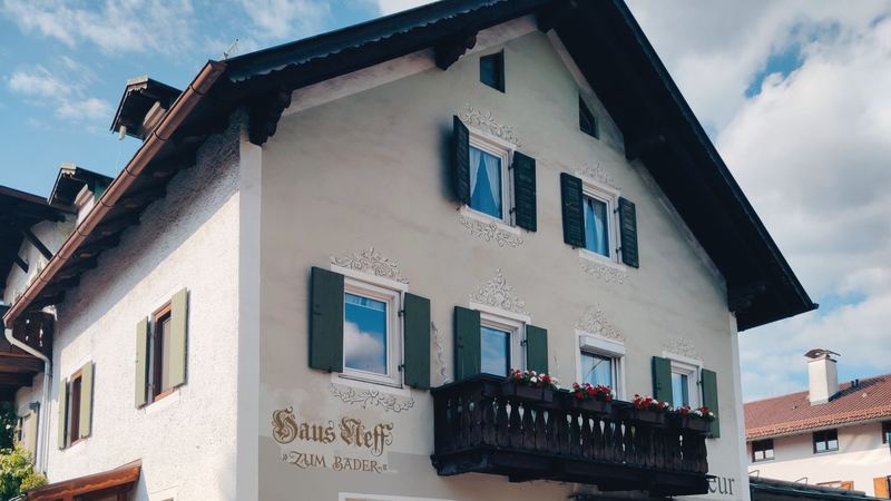 A Bavarian house with painted window frames, green shutters and a wooden balcony of red geraniums