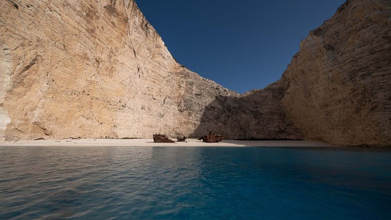 The shipwreck on the white beach of Navagio, Zakynthos, between tall limestone cliffs above turquoise water