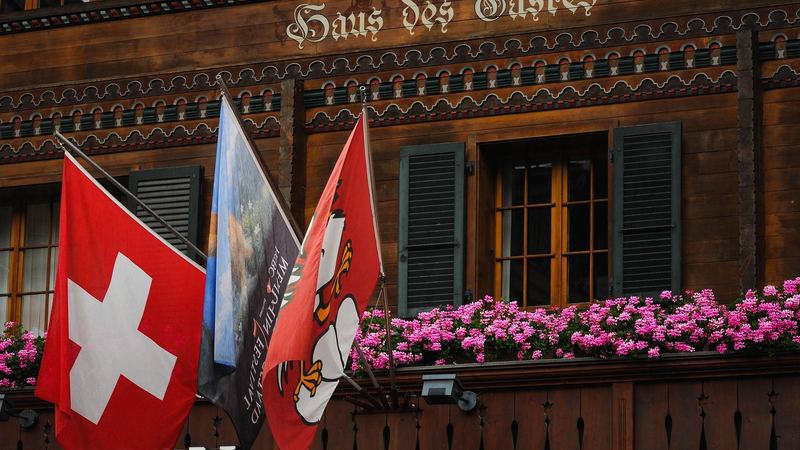 The Swiss, Menuhin Festival and Bernese flags on a carved wooden chalet with pink geraniums at the windows