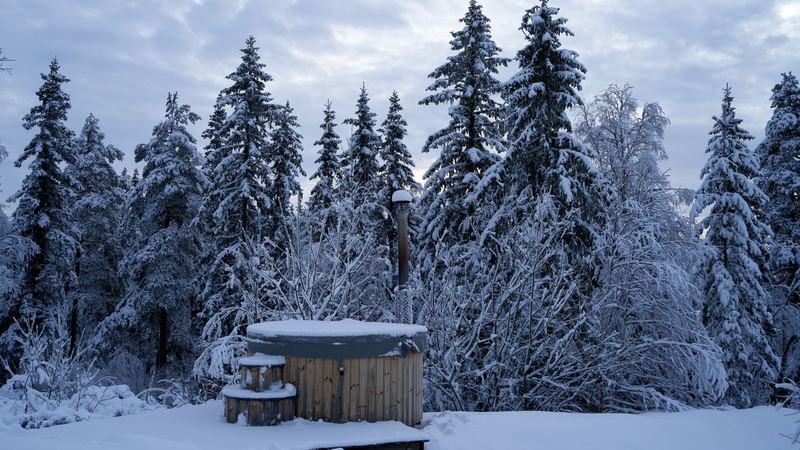 A wooden hot tub deep in snow among snow-laden firs