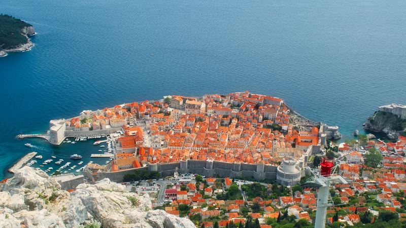 The red roofs and stone walls of Dubrovnik Old Town and its harbour, seen from Mount Srđ above the Adriatic
