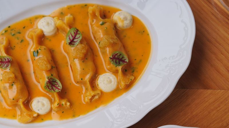Filled pasta in a golden sauce with herbs on fine white porcelain
