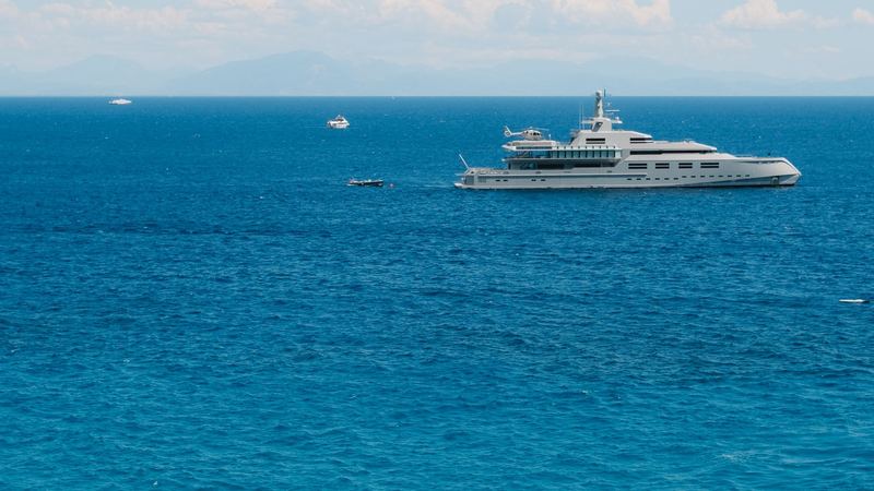 A superyacht with a helicopter on its deck at anchor off the Amalfi Coast in deep blue water