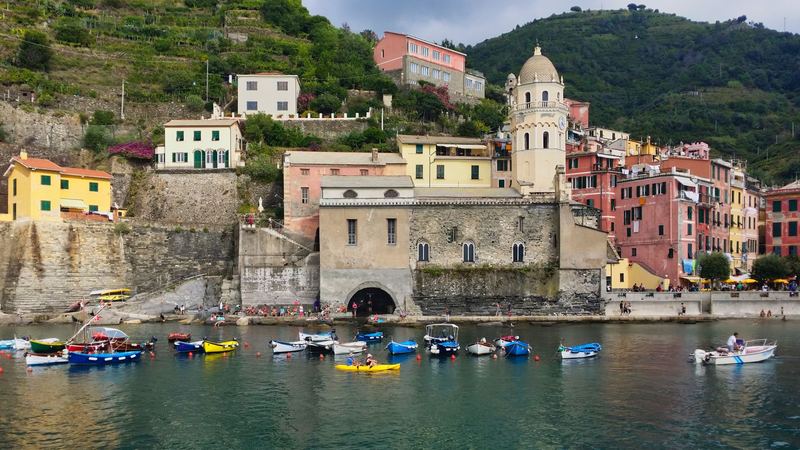 The pastel houses and church tower of Vernazza above a harbour of colourful boats in the Cinque Terre