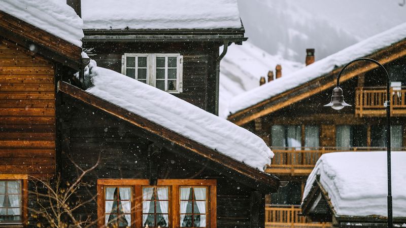 Old timber chalets with deep snow on their roofs and lace curtains at the windows, in falling snow