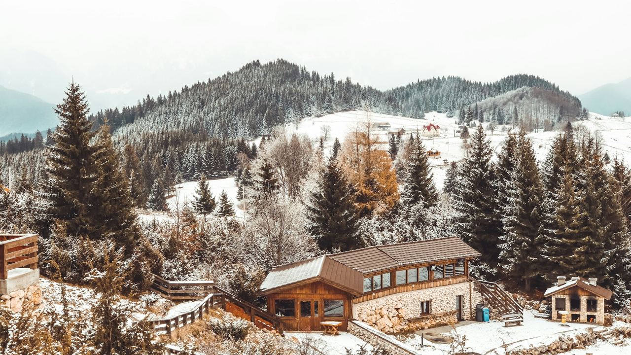 A timber and stone chalet among snowy firs, with mountain hamlets beyond