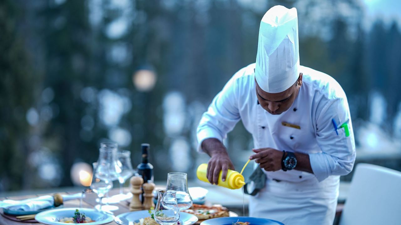 A chef finishing dishes at a table laid outdoors