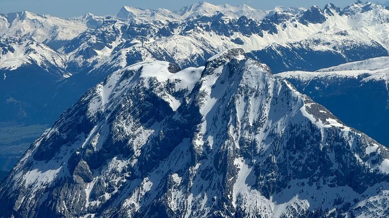 Snow-covered limestone peaks in spring sun, ranges of white summits beyond under a blue sky