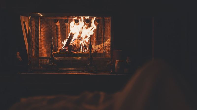 A log fire glowing behind a brass fire screen in a dark room at night