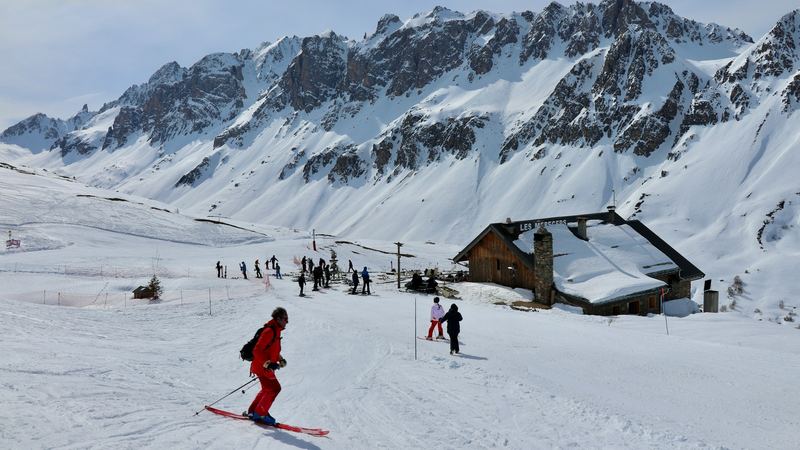 Skiers gathering at a stone and timber mountain restaurant below a wall of snowy peaks