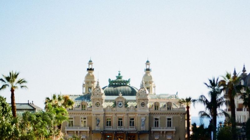 The domes and towers of the Casino de Monte-Carlo framed by palm trees, with the Hôtel de Paris to the right