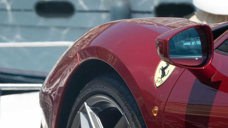 A deep red Ferrari parked on the quay in front of a superyacht in Port Hercule