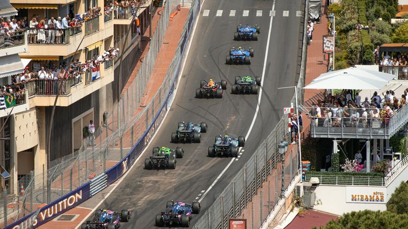 Formula 1 cars climbing the hill from Sainte-Dévote past crowded balconies at the Monaco Grand Prix