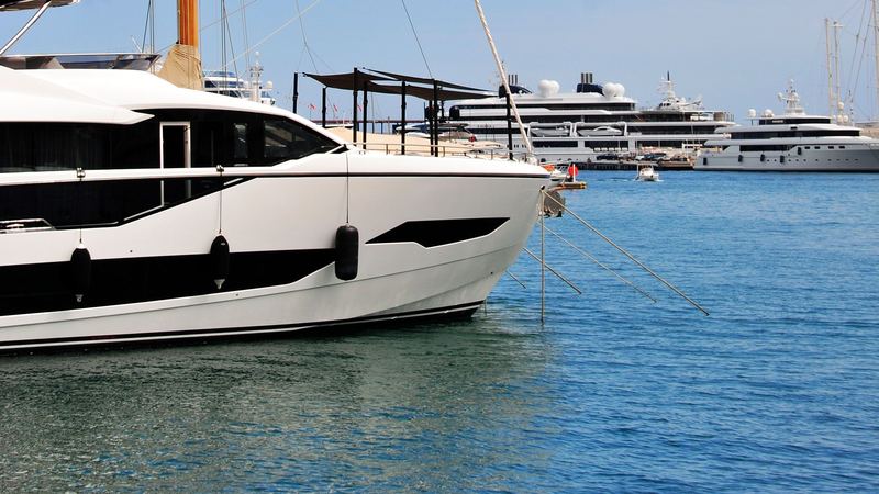 A sleek motor yacht beneath the wooden mast of a classic sailing yacht, superyachts across the harbour