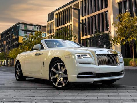 A white Rolls-Royce Dawn, roof down, below a sunset sky